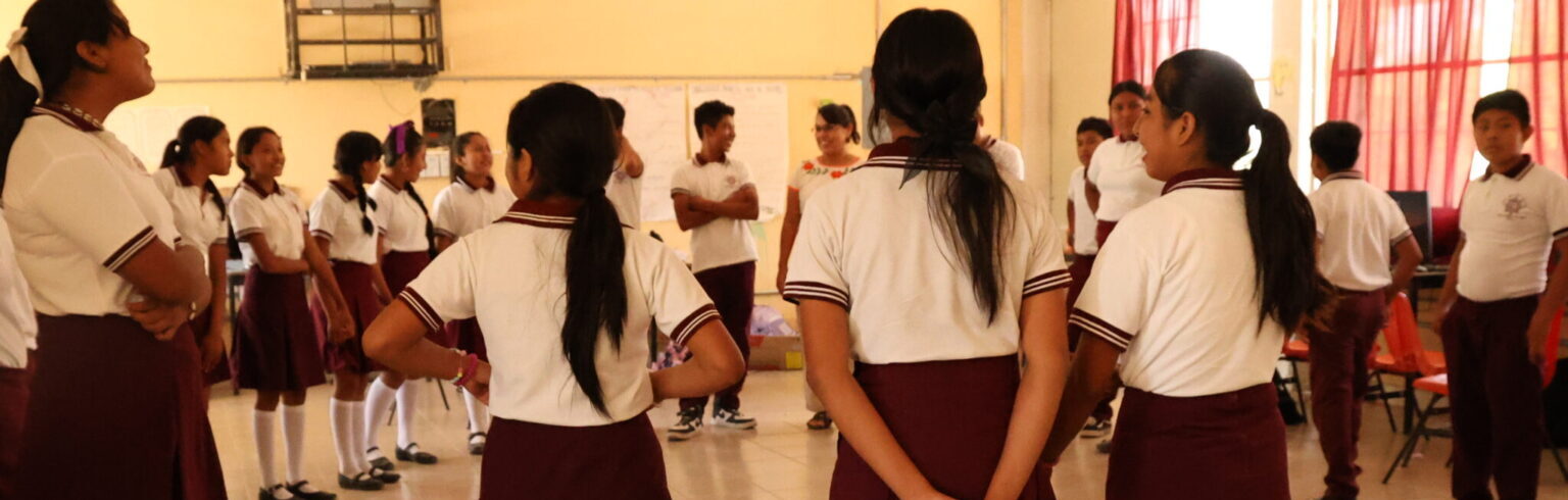 Fotografía donde aparecen jóvenes de secundaria parado en círculo en un salón de clases.
