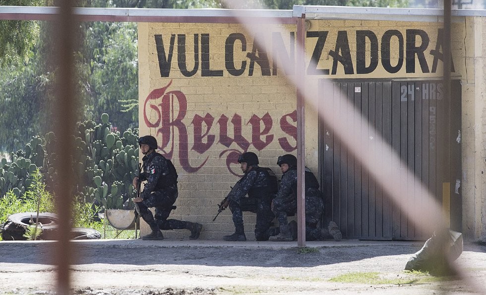 Tres hombres armados están de rodillas junto a un edificio