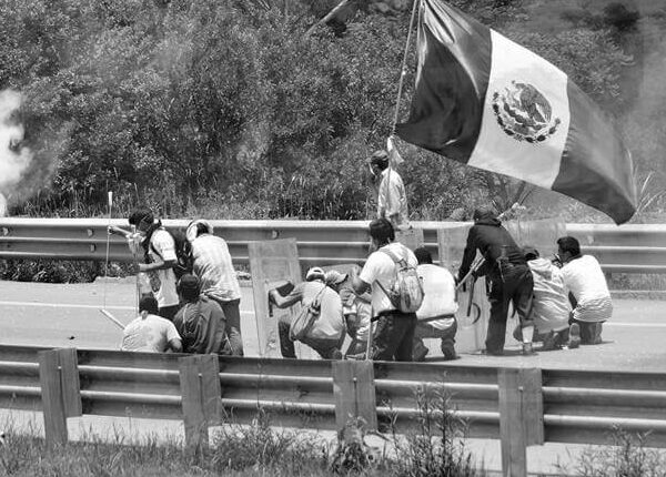 grupo de hombres que esquivan disparos y sostienen una bandera mexicana