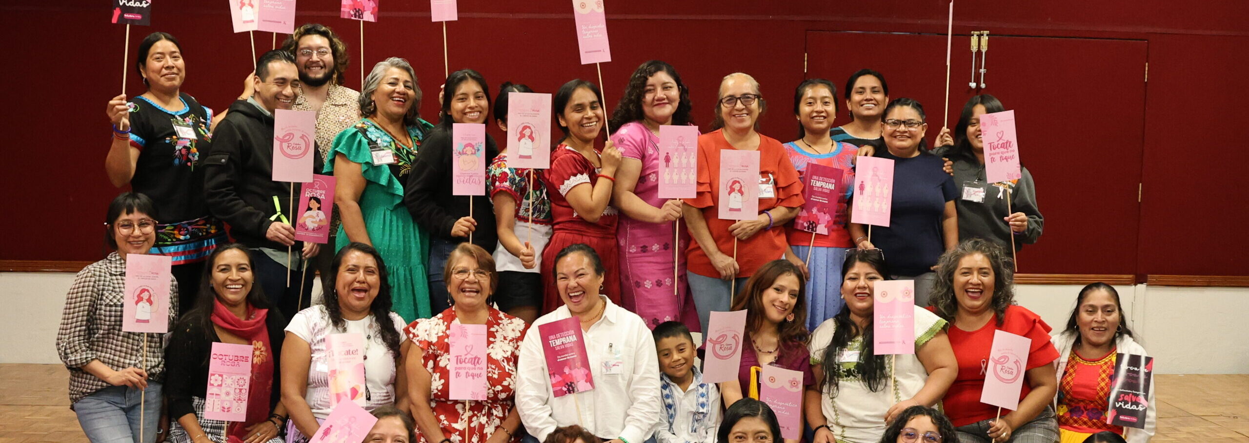 Foto grupal de mujeres sosteniendo carteles con mensajes de prevención del cáncer de mama